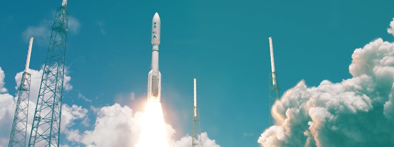 Rocket launching surrounded by clouds and a blue sky background. 