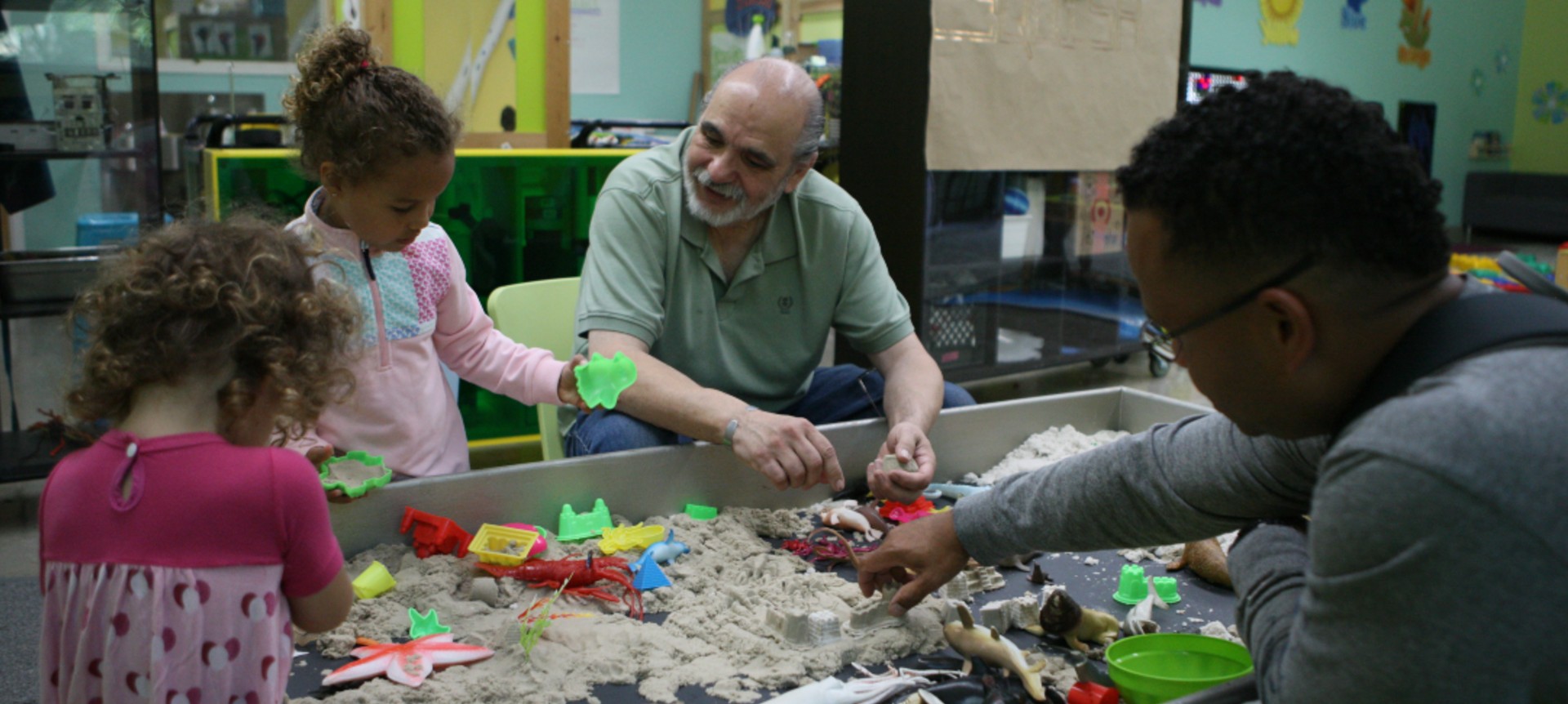 Two younger children and their chaperones playing with the indoor sandbox. 