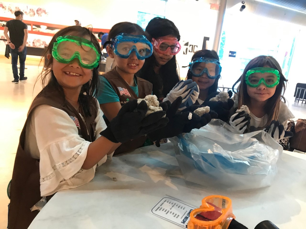A group of young visitors wearing goggles and gloves completing a workshop and posing for a picture. 