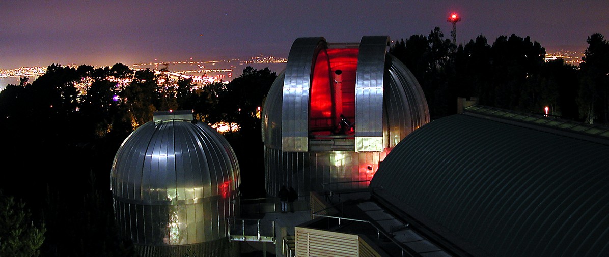 Aerial view of two of our telescope domes, with a background of the night sky and Bay Bridge skyline. 